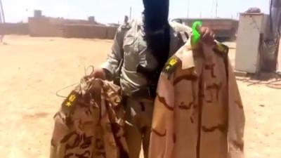 Armed member of ISIL holding up Iraqi soldier uniforms before tossing them on the ground-Mosul, Iraq.